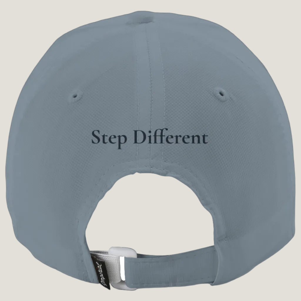The back of a slate blue-gray baseball cap with the text 'Step Different' embroidered in blue on the center back, featuring an adjustable hook-and-loop strap with a silver metal buckle.